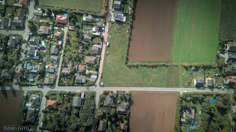 Vogelperspektive auf eine Wohnsiedlung mit einzelnen Häusern, Straßen und landwirtschaftlichen Flächen.