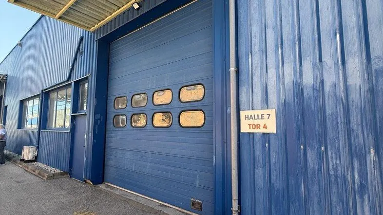 Blaue Wellblechfassade einer Industriehalle mit großem Rolltor und Beschilderung, zeigt den Eingangsbereich.