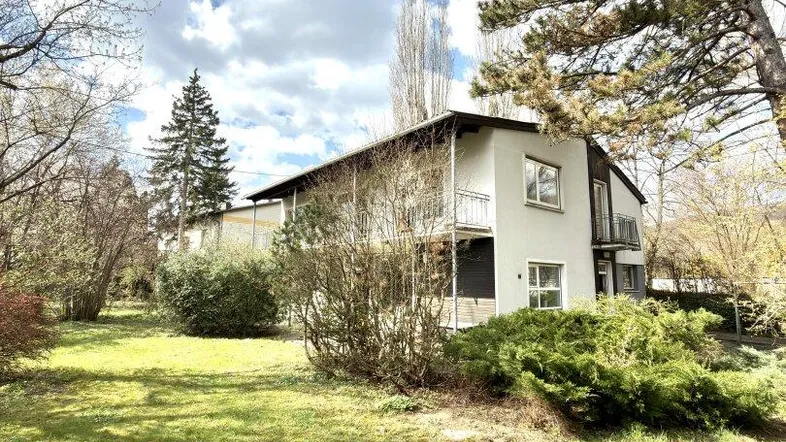 Großzügiger Gartenbereich mit Rasenfläche und Blick auf das Wohnhaus unter bewölktem Himmel.