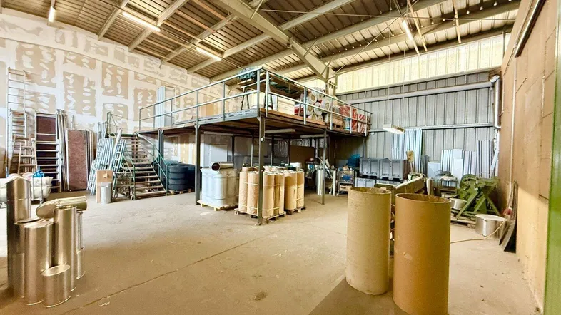 Geräumige Lagerhalle mit hoher Decke, Zwischengeschoss und gestapelten Materialien für industrielle Nutzung.