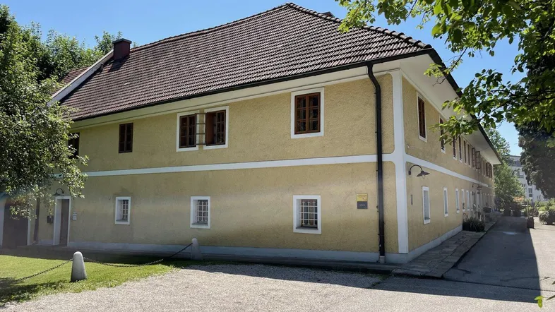 Traditionelles Gebäude mit gelber Fassade und Ziegeldach unter blauem Himmel an einem sonnigen Tag.