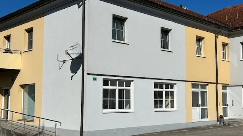 Außenansicht des Gebäudes mit gelb-grauer Fassade und einer barrierefreien Rampe am Eingangsbereich.