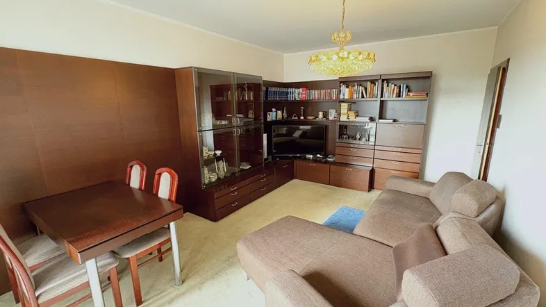 Geräumiger Wohn-Essbereich mit beigem Teppichboden, großem Sofa und dunkler Schrankwand.
