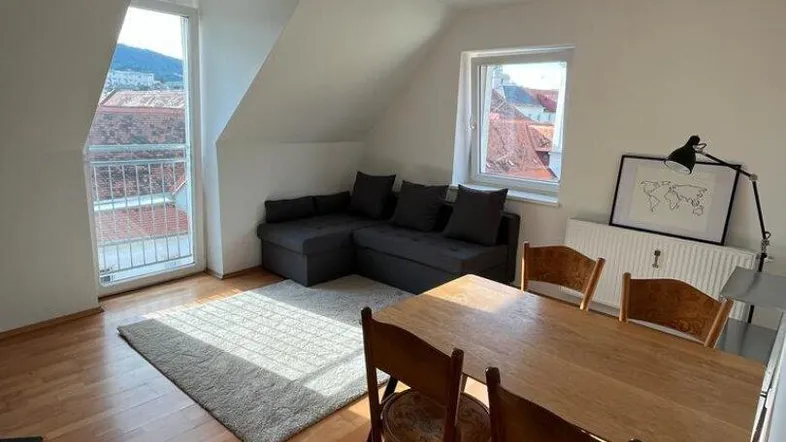 Helles Wohn- und Esszimmer im Dachgeschoss mit Holzboden, gemütlichem Sofa und Zugang zum Balkon.