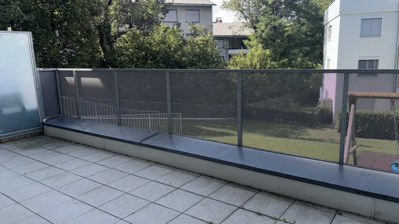 Große geflieste Terrasse mit Metallgeländer und Blick ins Grüne.
