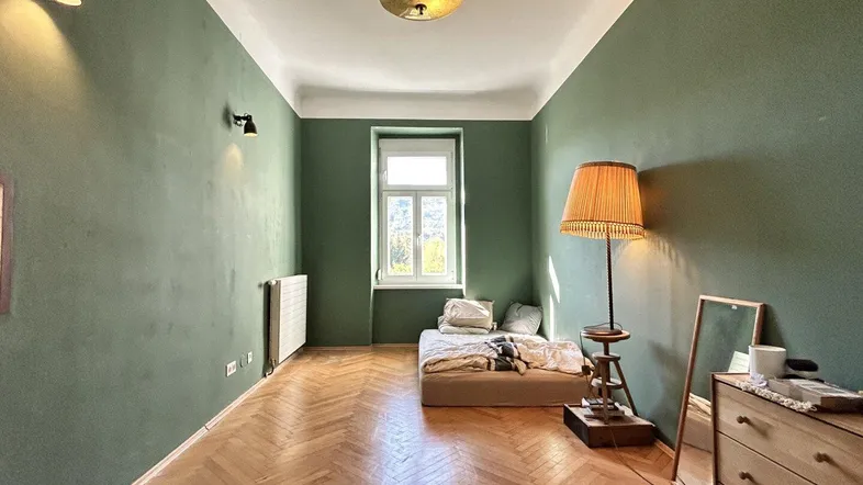 Helles Schlafzimmer mit grünen Wänden, Fischgrätparkett und einem Fenster mit Bergblick.