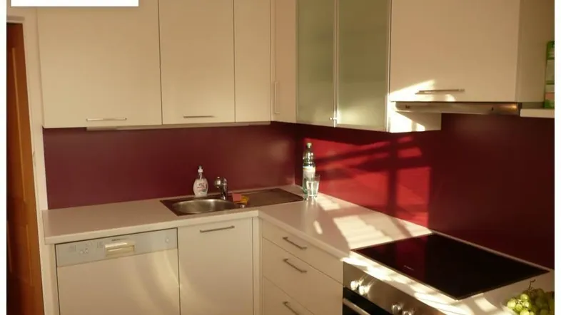 Moderne Einbauküche mit weißen Schränken, roter Rückwand und integrierten Geräten.