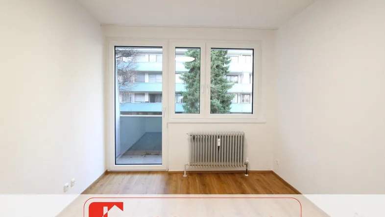 Helles Zimmer mit Laminatboden und Zugang zu einem Balkon, ausgestattet mit einem Heizkörper.