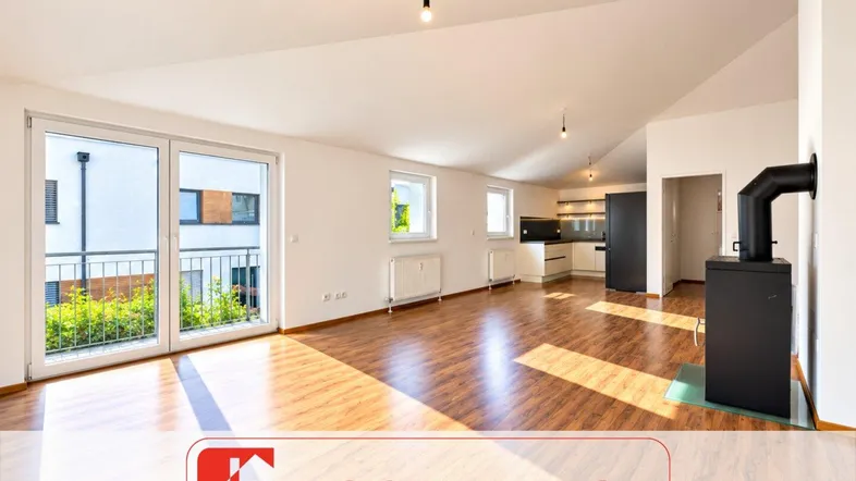 Heller, offener Wohnbereich mit Laminatboden, Kaminofen und Zugang zu einem Balkon.