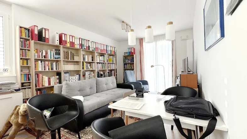 Helles Wohnzimmer mit umfangreichen Bücherregalen, einem bequemen Sofa und einem Arbeitstisch.