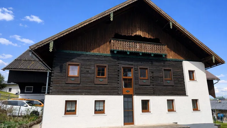 Traditionelles Holzhaus mit weiß getünchter Fassade und Holzbalkon unter blauem Himmel.