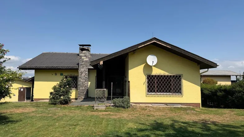 Gelbes Einfamilienhaus mit Satteldach und Steinkamin vor einem grünen Rasen.