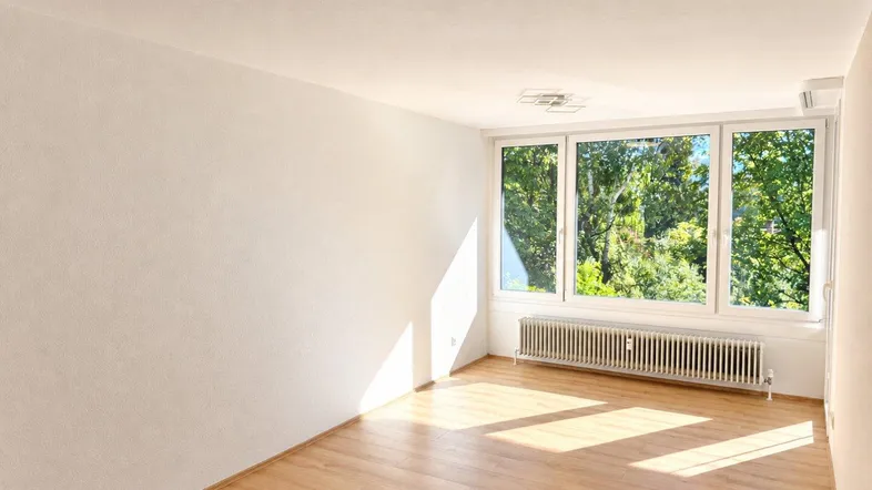 Helles Zimmer mit großen Fenstern, Holzboden und viel natürlichem Licht, ideal als Wohn- oder Schlafzimmer.