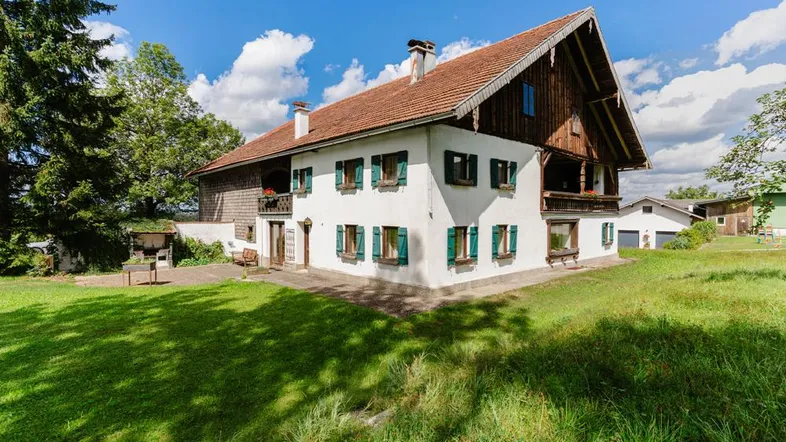 Traditionelles Landhaus mit weißer Fassade, grünen Fensterläden und großem Gartenbereich unter blauem Himmel.