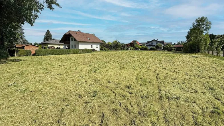 Weitläufiges Grundstück mit frisch gemähter Wiese und umliegenden Wohnhäusern unter blauem Himmel.