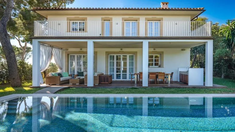 Elegantes Haus mit großem Pool und überdachtem Außenbereich, umgeben von grüner Natur.