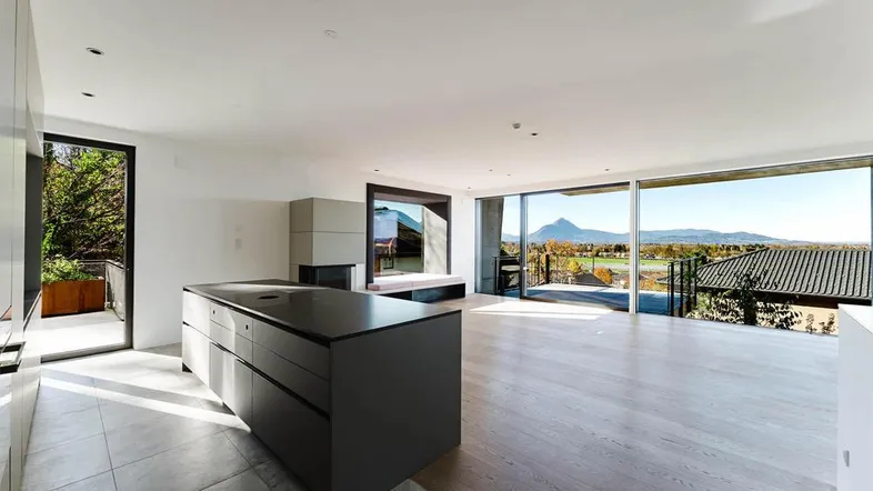 Heller offener Wohnbereich mit moderner Kücheninsel, Kamin und Panoramafenstern mit Bergblick.