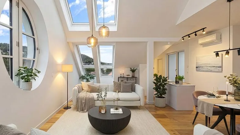 Helles, offenes Wohn- und Esszimmer mit Dachschrägen, modernen Möbeln und großen Dachfenstern mit Ausblick.