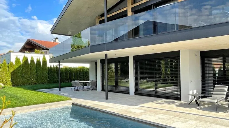 Moderne Villa mit Pool, Terrasse und Gartenbereich unter blauem Himmel.