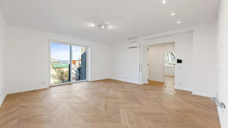Helles Wohnzimmer mit elegantem Fischgrätparkett, weißen Wänden und Zugang zu einem Balkon.