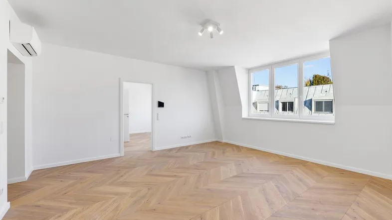 Helles, leeres Zimmer mit modernem Fischgrätparkett und großen Fenstern, die viel Tageslicht hereinlassen.