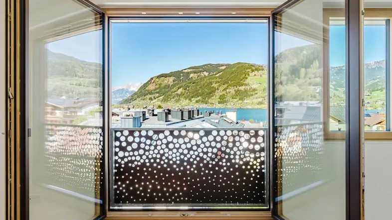 Heller Innenraum mit geöffneten Glastüren, die einen atemberaubenden Blick auf den See und die Berge freigeben.