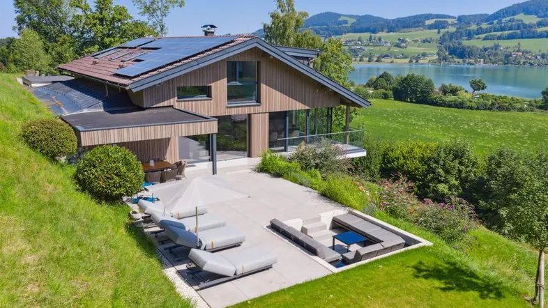 Modernes Haus mit großer Terrasse, Sonnenliegen und atemberaubendem Blick auf den See und die umliegende Landschaft.