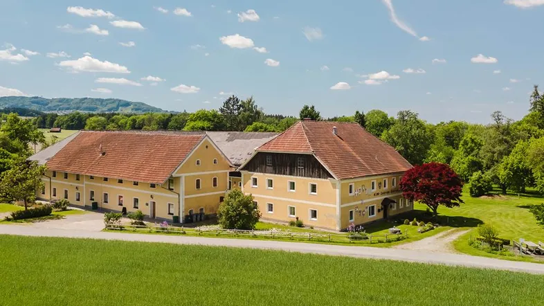 Großes, traditionelles Gebäudeensemble mit gelber Fassade und roten Ziegeldächern in ländlicher Umgebung.