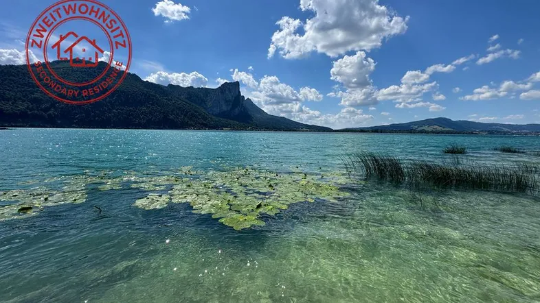 Malerischer Blick auf einen klaren See mit majestätischen Bergen im Hintergrund unter blauem Himmel.