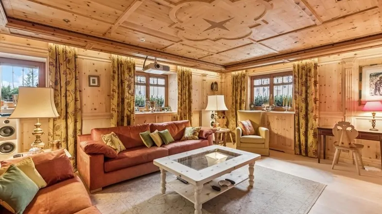 Gemütliches Wohnzimmer im alpinen Stil mit Holzvertäfelung, Deckenprojektor und bequemen Sofas.