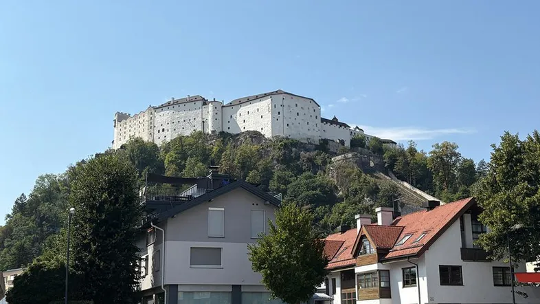 Blick auf eine historische Festung auf einem Hügel mit Wohnhäusern im Vordergrund unter blauem Himmel.