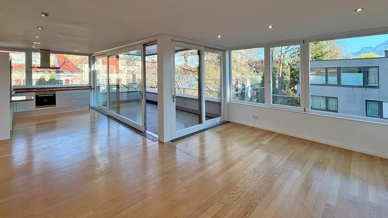 Heller, offener Wohn- und Essbereich mit Parkettboden, integrierter Küche und Zugang zum Balkon.