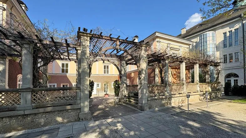 Historischer Gartenbereich mit Pergola und gepflastertem Weg, umgeben von eleganten Gebäuden.