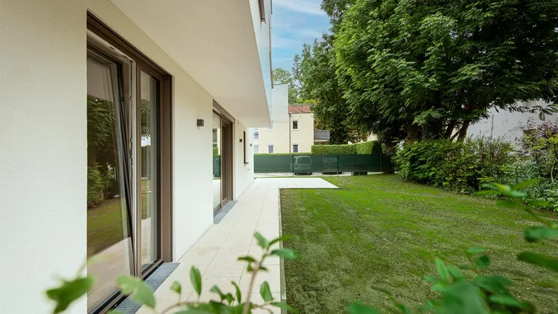 Moderne Gebäudefassade mit großen Fenstern, angrenzender Terrasse und gepflegtem Rasenbereich.
