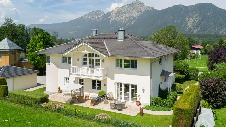 Elegantes Haus mit großer Terrasse und Garten, umgeben von einer malerischen Berglandschaft.