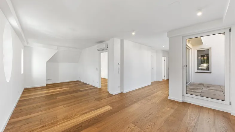 Helles Zimmer mit Holzboden, runden Fenstern und Zugang zu einem Außenbereich.