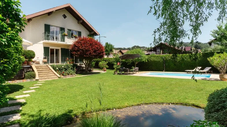 Großer Garten mit Swimmingpool, Teich und gepflegter Rasenfläche vor dem Haus an einem sonnigen Tag.