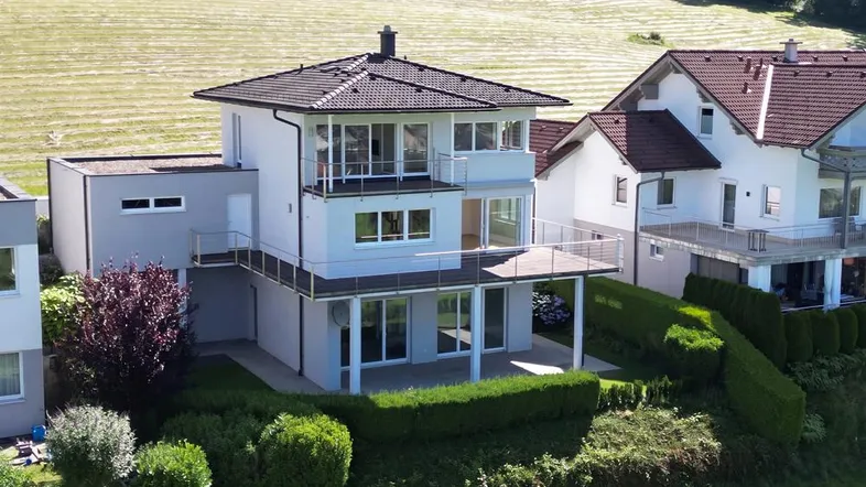 Modernes Einfamilienhaus mit mehreren Balkonen, Terrasse und Blick ins Grüne.