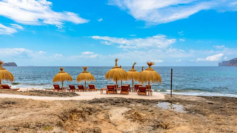 Sonniger Strandabschnitt mit Strohschirmen und Liegestühlen am Meer, ideal zum Entspannen.