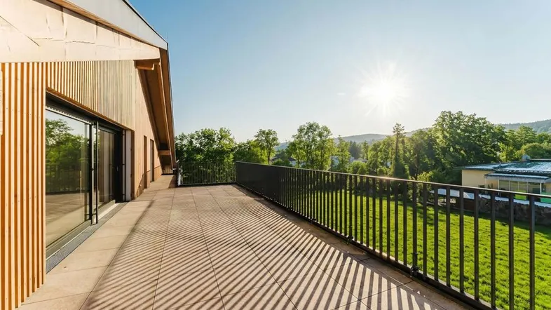 Große, sonnige Terrasse mit Blick ins Grüne und moderner Holzfassade des Gebäudes.
