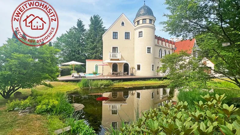 Elegantes Anwesen mit Turm, Teich und weitläufiger Terrasse, umgeben von üppigem Grün.