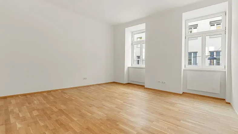 Helles und geräumiges Zimmer mit Parkettboden und zwei großen Fenstern, ideal als Wohnbereich.
