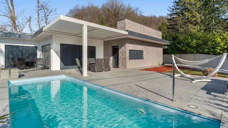 Moderne Villa mit Swimmingpool, großer Terrasse und Gartenbereich unter blauem Himmel.
