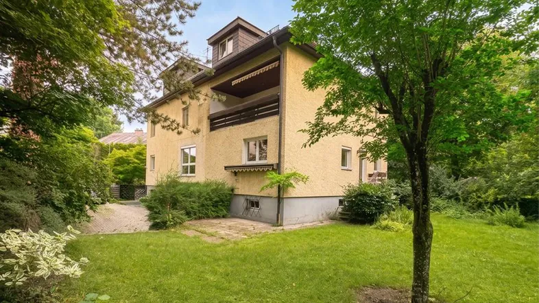 Gelbes Mehrfamilienhaus mit Balkon, Dachgauben und großem Gartenbereich.