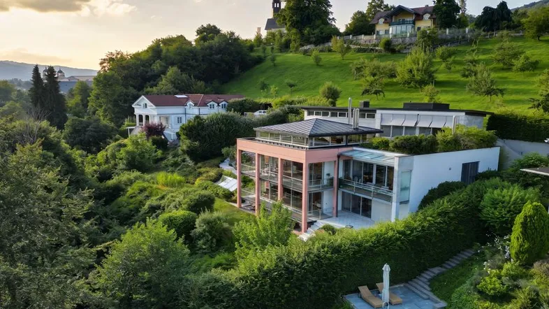 Moderne Villa am Hang mit Pool, umgeben von üppigem Grün und Fernblick auf die Landschaft.