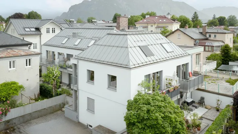 Modernes Mehrfamilienhaus mit Balkonen, Gartenbereich und beeindruckendem Bergblick im Hintergrund.