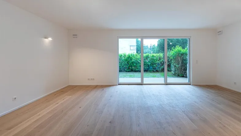 Heller, leerer Raum mit Holzboden und großzügigem Zugang zum Gartenbereich durch große Schiebetüren.