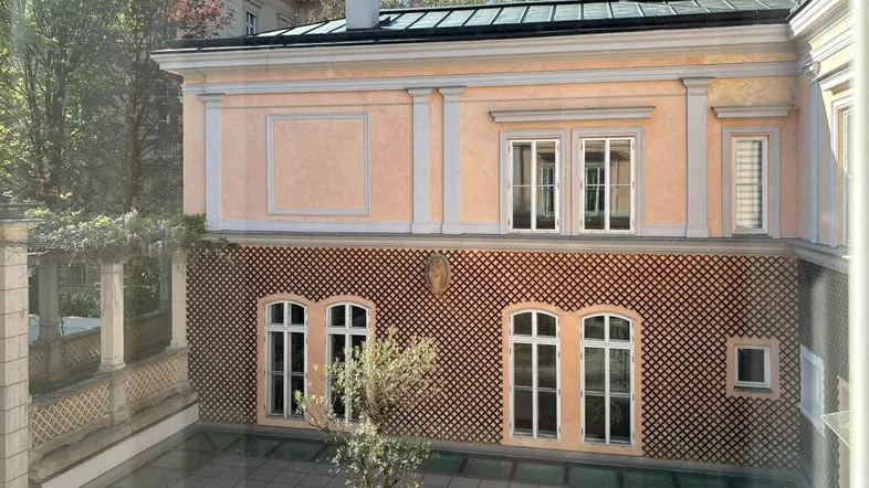 Blick aus dem Fenster auf einen charmanten Innenhof mit gepflastertem Boden und einem kleinen Baum.