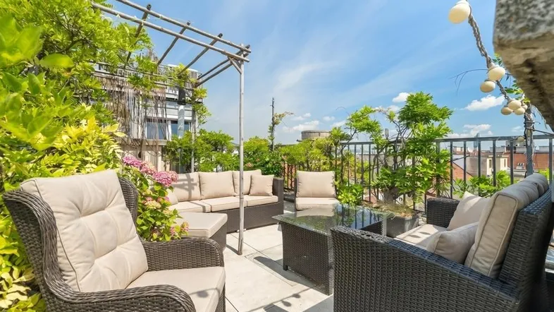 Geräumige Dachterrasse mit bequemen Loungemöbeln, üppiger Bepflanzung und weitem Stadtblick unter blauem Himmel.