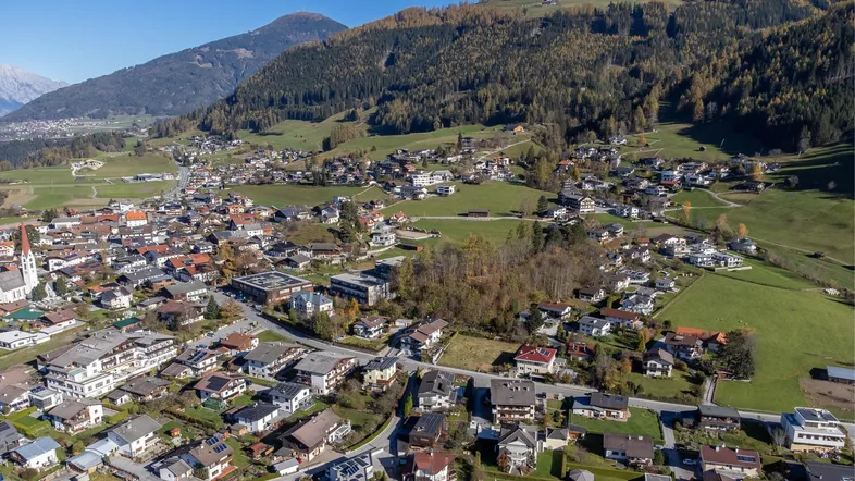 Weitläufige Luftaufnahme eines Dorfes in den Bergen mit vielen Wohnhäusern und grüner Landschaft.